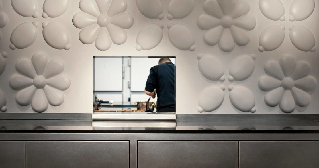 A Person Standing In A Room With White Walls And A Counter With A Window And A Person Sitting