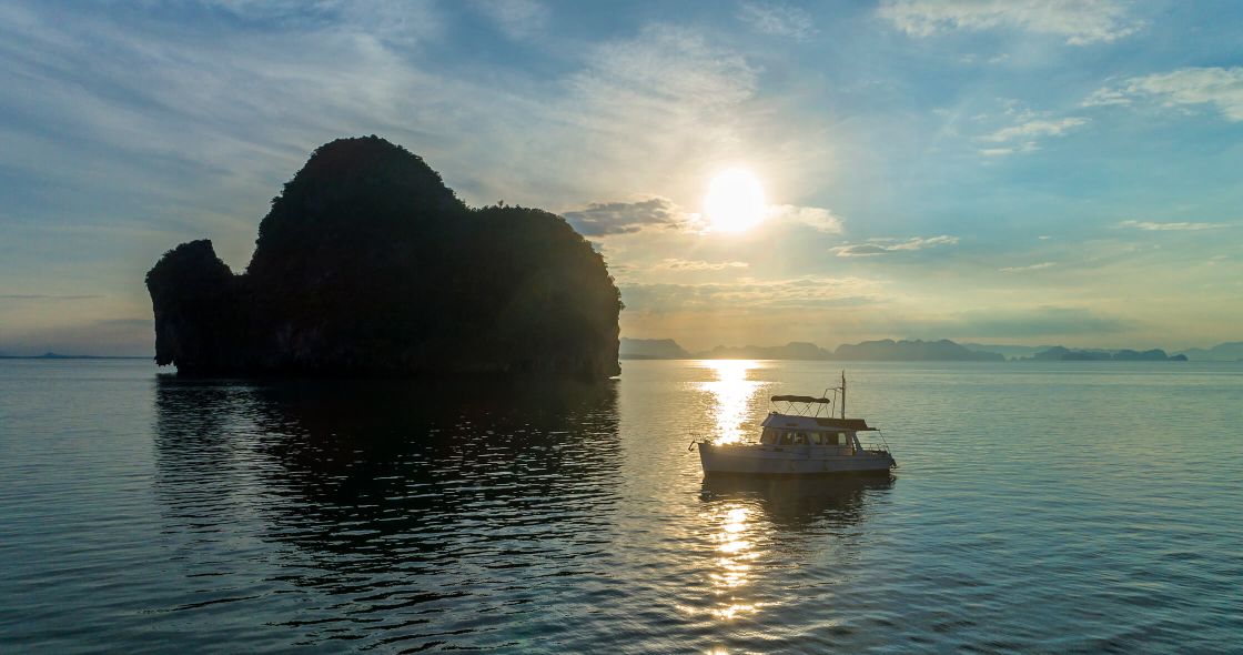 A Boat In The Water With A Large Rock In The Background